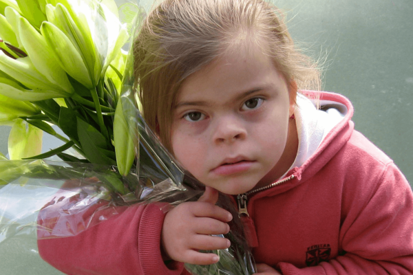 Down syndrome little girl carry a bouquet of flowers.