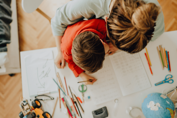 Mother homeschooling her child using lots of coloured pencils and paper.