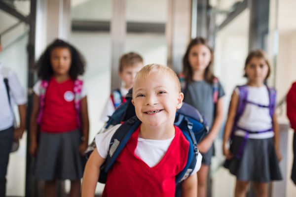 A young down syndrome boy smiling while walking in a school hallway.