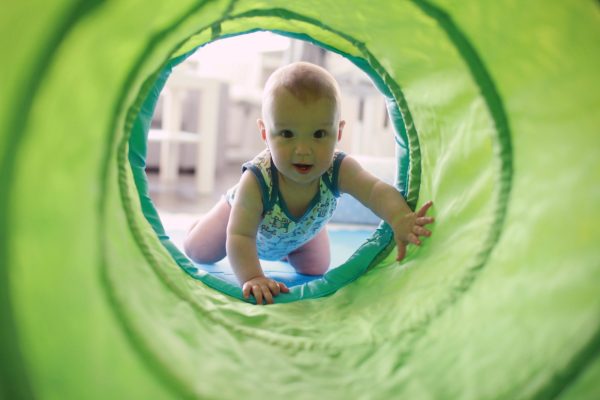 Cute baby crawling through a green play tunnel.